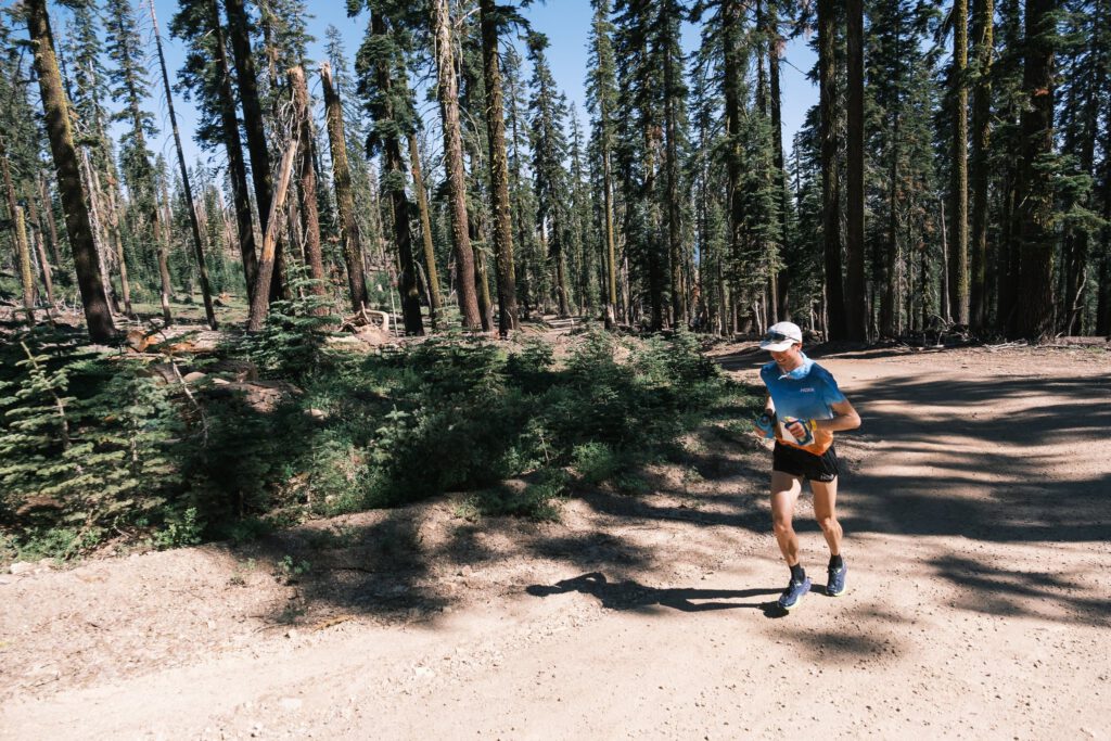 Adam Peterman running on a dirt fire road in a forest.