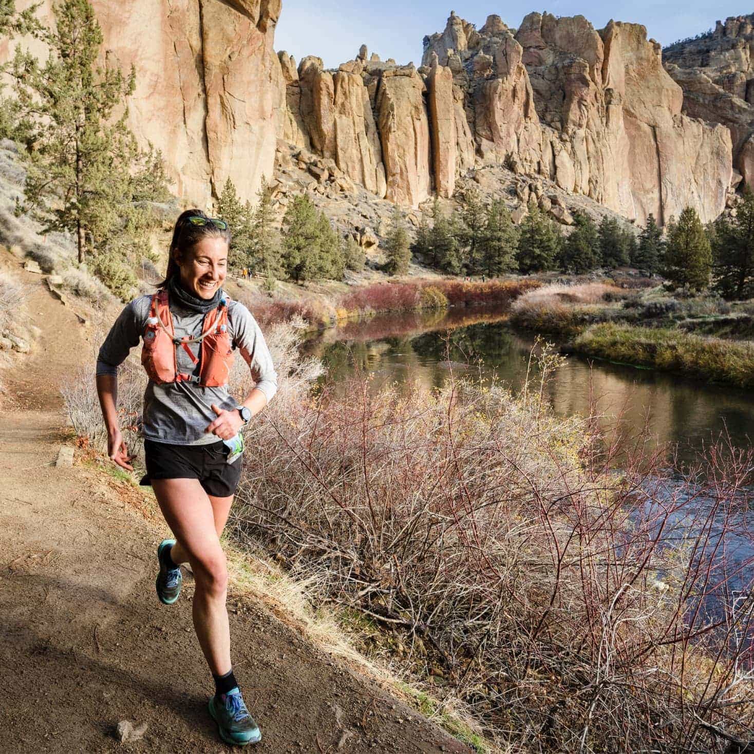 Laura MacCarley runs at Smith Rock near Bend, OR with a river and cliffs in the background.