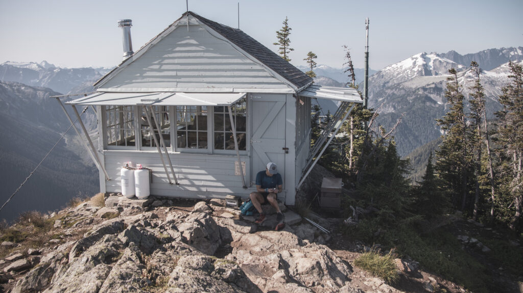 A trail runner sits and writes outside of an old fire lookout tower